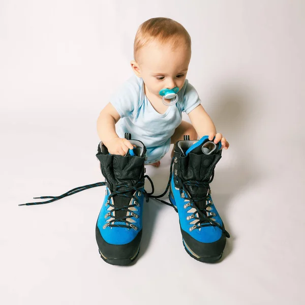 little boy sits near mountaineering boots