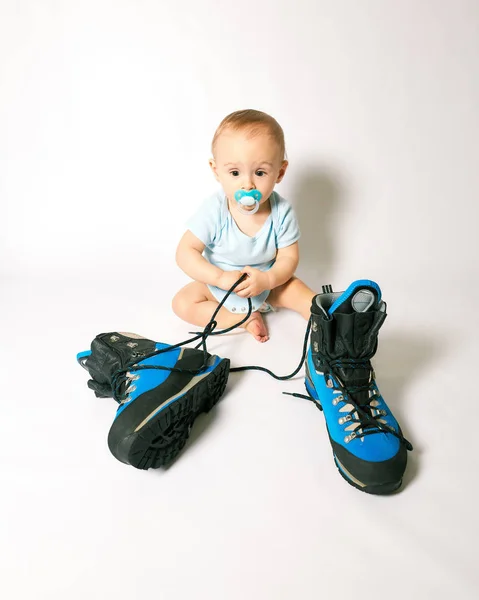 little boy sits near mountaineering boots