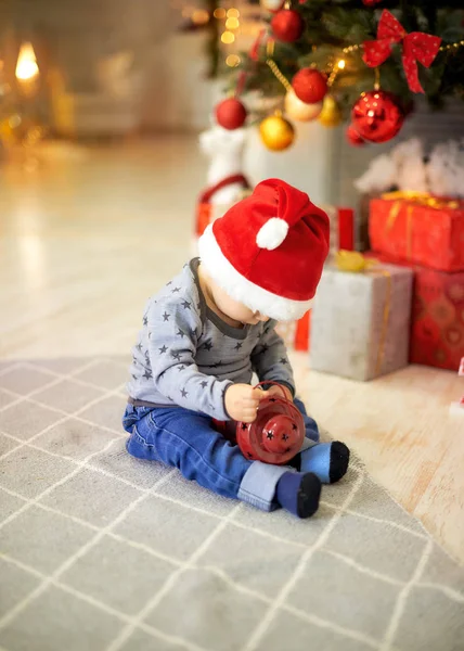 Mały chłopiec siedzi na tle choinki — Zdjęcie stockowe