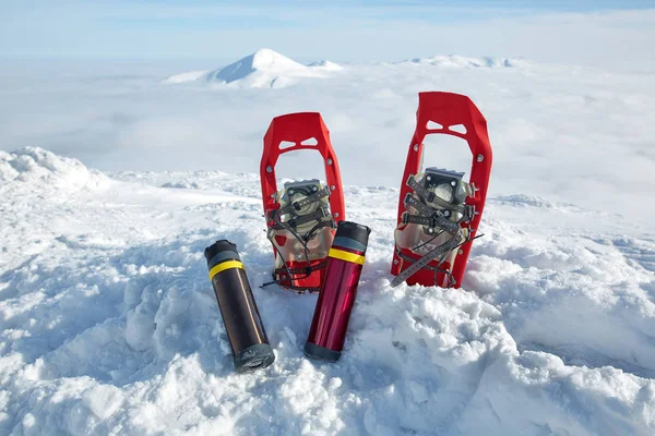 红色雪鞋和两个热水瓶在云层上方雪山的背景上 — 图库照片
