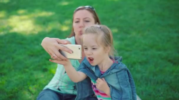 Kleines Mädchen mit Mutter, die sich in einem Park ausruht, macht Selfie. — Stockvideo