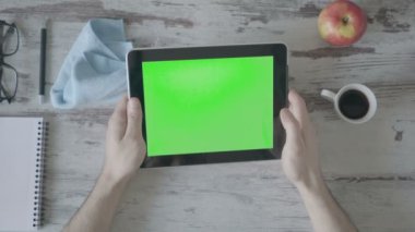 Tablet pc ile yeşil boş perde ahşap arka plan üzerinde tutan eller