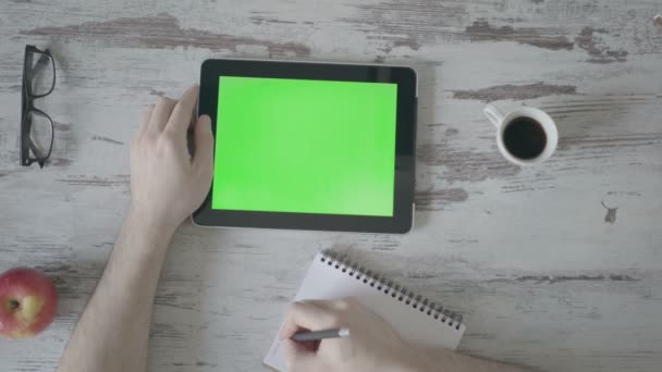 Manos masculinas hacen notas en un cuaderno, a continuación hay una tableta con una pantalla verde — Vídeo de stock