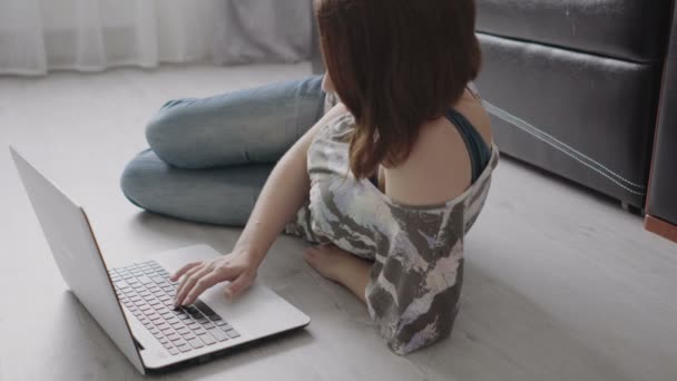 Hübsches junges Mädchen liegt mit Laptop auf dem Boden. — Stockvideo