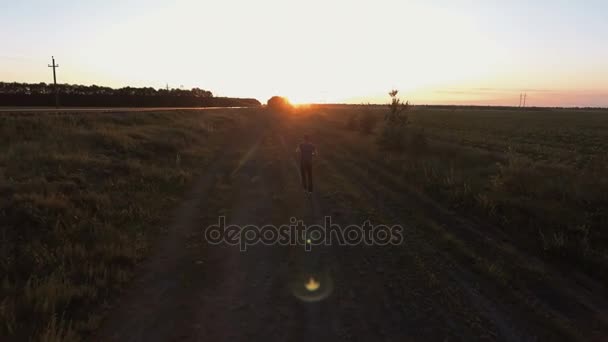 Aerial. Running athlete man. on road outside in green field. — Stock Video