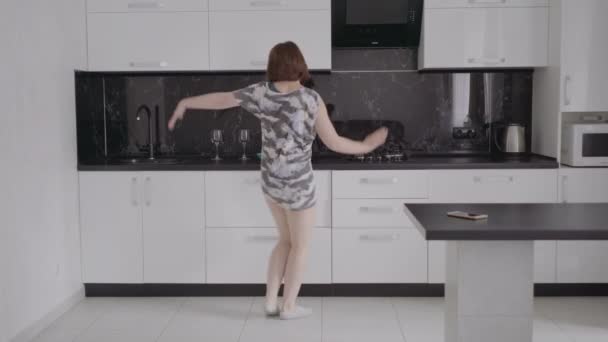 Lustige junge Frau, die morgens im Schlafanzug in der Küche tanzt. — Stockvideo