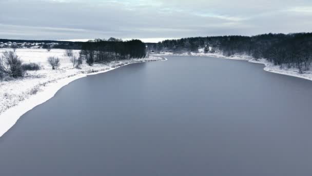 Vuelo sobre el bosque de nieve y el lago congelado en la primera nieve — Vídeo de stock