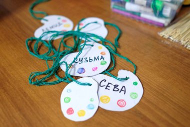 Homemade baby badges on a string. Identification of children at the event. Words: SEVA, KUZMA