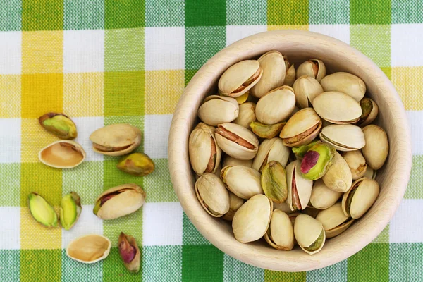 Pistachio nuts in wooden bowl on checkered cloth — Stock Photo, Image