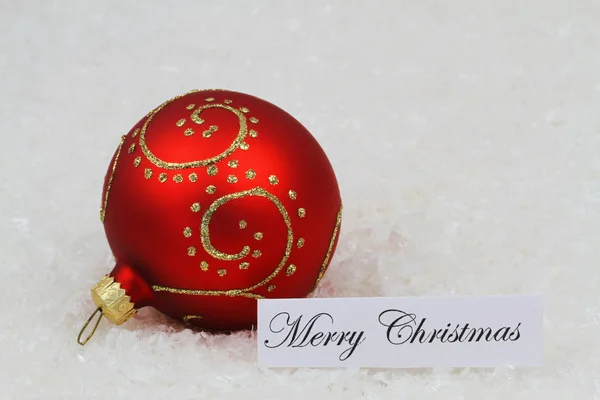 Feliz tarjeta de Navidad con adorno rojo con brillo en la superficie nevada —  Fotos de Stock