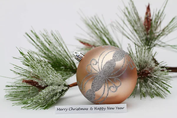 Frohe Weihnachten und ein glückliches neues Jahr Karte mit cremefarbener Christbaumkugel und Kiefer mit Schneeflocken bedeckt — Stockfoto