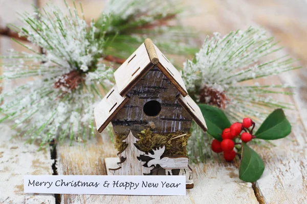 Feliz Navidad y Feliz Año Nuevo con casa de madera en miniatura y pino cubierto de copos de nieve — Foto de Stock