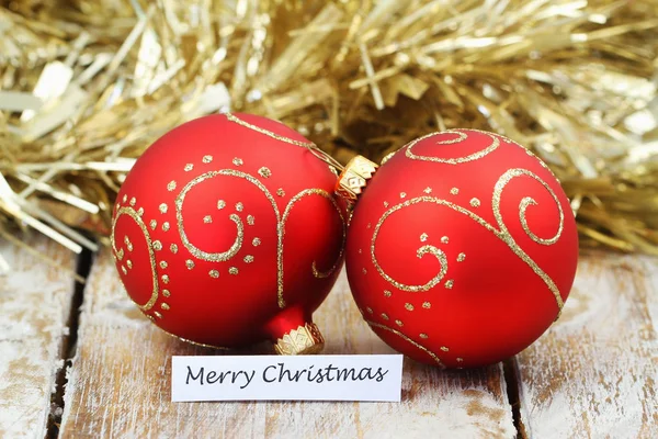 Frohe Weihnachtskarte mit roten Kugeln und goldener Kette auf Holzoberfläche — Stockfoto