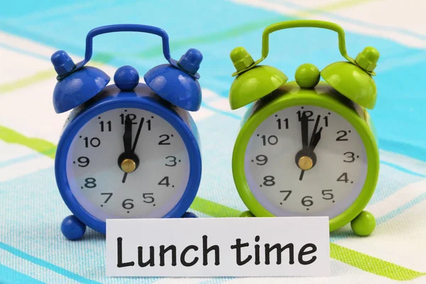 Cartão de hora de almoço com dois relógios em miniatura mostrando doze e uma horas — Fotografia de Stock