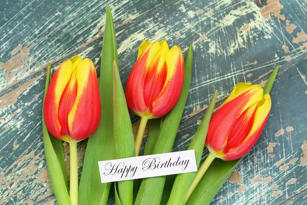 Tarjeta de cumpleaños feliz con tulipanes rojos y amarillos en la superficie de madera rústica —  Fotos de Stock