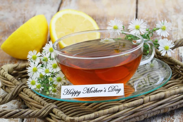 Tarjeta del día de la madre feliz con taza de té y flores de manzanilla en bandeja de mimbre —  Fotos de Stock