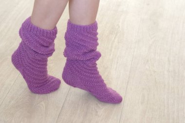 Bej bir arka planda yüksek örülmüş menekşe rengi çoraplı kadın bacakları.