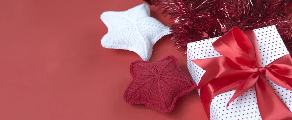 Christmas banner with gift box, tinsel, and knitted stars. Gift concept for needlewoman on a red background