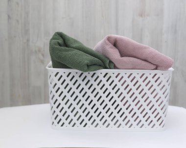 Beyaz plastik sepet ve arka planda çok renkli temiz havlular.