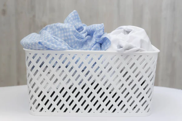 Blue and white dirty things in a white plastic laundry basket on a gray wall background. Washing, home cleaning