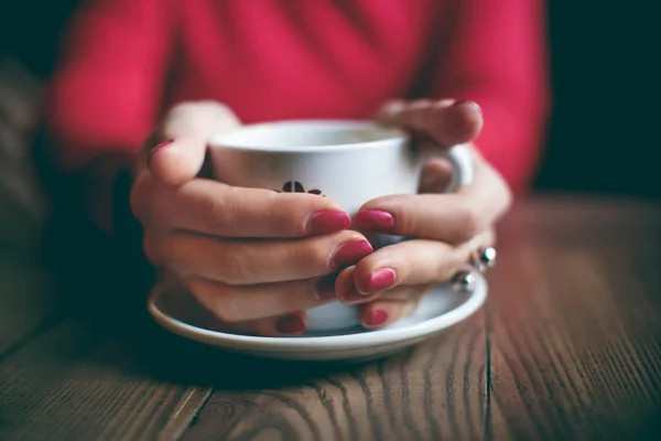 Woman with red nails in red dress keep her arms on the coffee cup