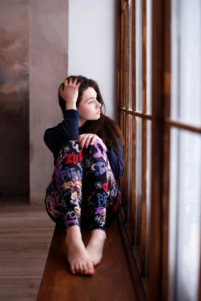 Beautiful girl sitting on  the windowsill in a calm pose