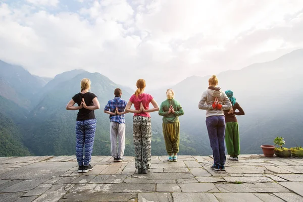 Group of people doing standing yoga exercise. Namaste behind the back, yoga asana on beautiful mountain landscape background