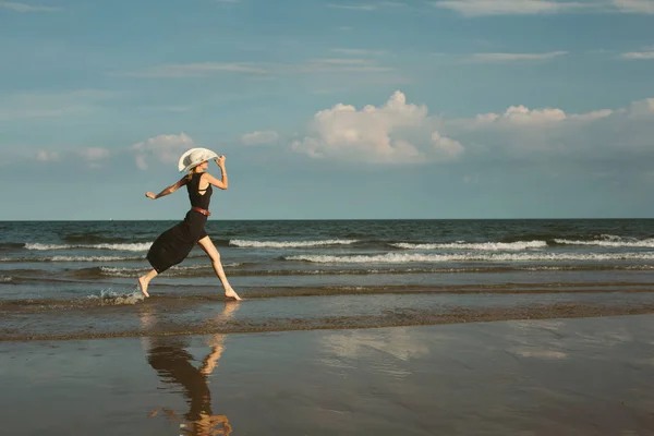 Femme en grand chapeau blanc courant par la mer bleue — Photo