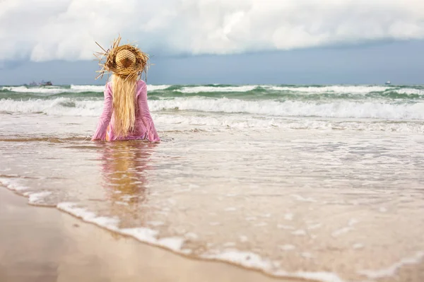 Deniz kıyısında oturan hasır şapkalı sarışın kadın — Stok fotoğraf