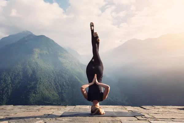 Mujer joven haciendo ejercicio de Yoga complejo de cabeza con Namaste asana. Increíble paisaje de Yoga en hermosas montañas —  Fotos de Stock