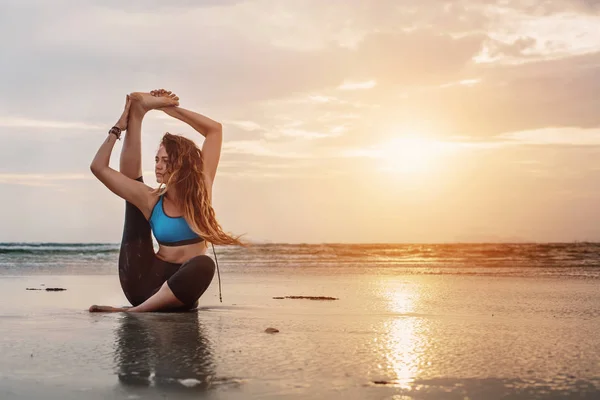 Gün batımında plajda yoga yapan genç bir kadın. — Stok fotoğraf