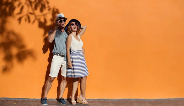 Casal sorridente perto da parede laranja — Fotografia de Stock