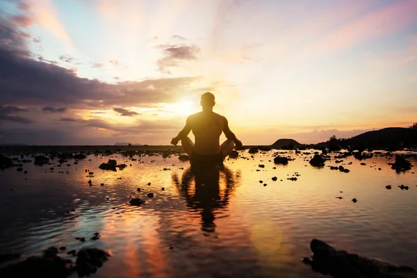 Silueta de joven sentado practicando yoga en la playa al atardecer — Foto de Stock