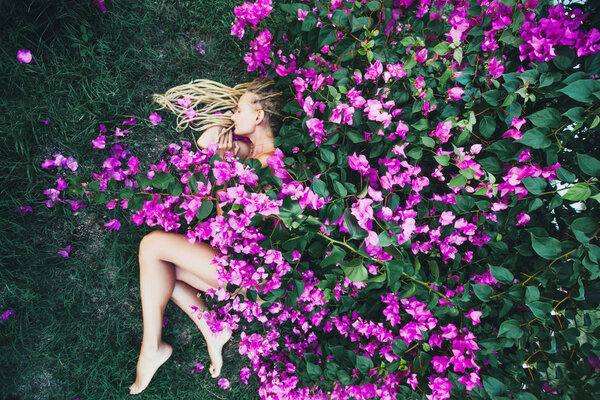 Beautiful female sleeping outdoor in nature under bougainvillea flowers