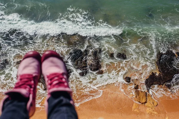 Legs wearing pink sneakers with ocean cliff view background