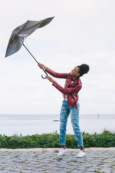 Young female with broken  umbrella on sea shore. Black model mixed race with african hairstyle