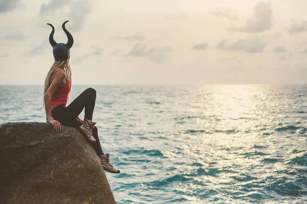 Boynuz Maskeli Bir Kadın Uçurum Kıyısında Oturuyor Günbatımının Tadını Çıkarıyor — Stok fotoğraf