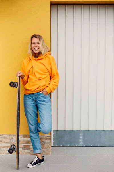 Уличный Портрет Положительной Молодой Женщины Оранжевой Толстовке Скейтбордом Городе — стоковое фото