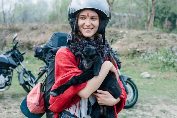 Travelling by motorcycle young woman wearing helmet keeping black lamb and smiling. Long motor travel in mountains