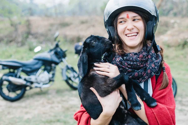 Travelling by motorcycle young woman wearing helmet keeping black lamb and smiling. Long motor travel in mountains