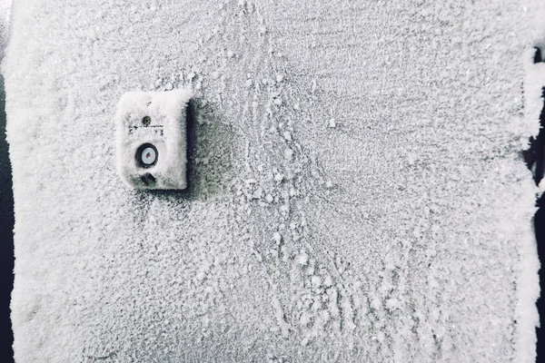 Frozen intercom button on door in building, cold snowy winter on the north