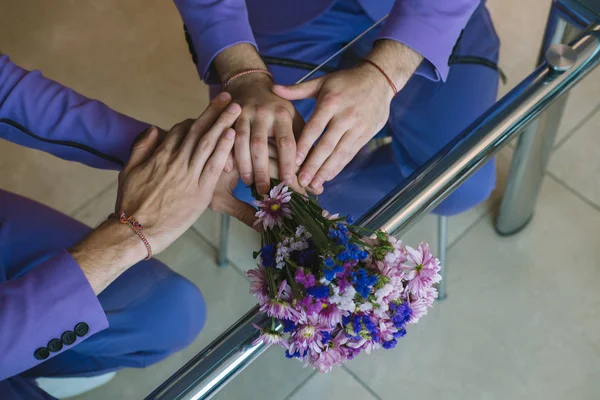 Hands of to partners homosexual couple on wedding day. Wedding bouquet of purple flowers on the table