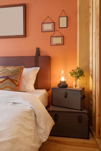 modern interior design details, studio apartment with double bed and wooden decor. Orange  color wall, empty frame, kerosene lamp and chests boxes in decoration