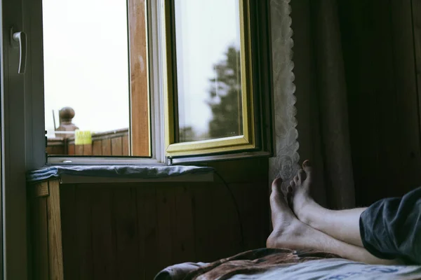 Summer Morning at home near open window, male legs on the bed in wooden house