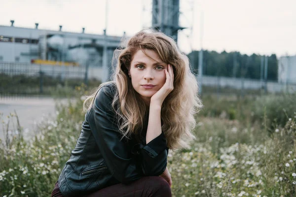 beautiful female traveling by car wearing leather jacket standing outdoor. Industrial landscape on background