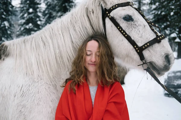 Beautiful woman with white horse in winter fir forest