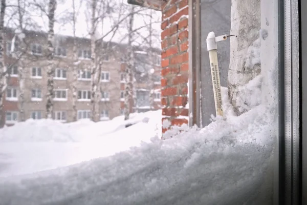 Old mercury outdoor street thermometer with celsius on heavy snowy window at winter day in city