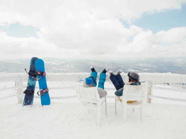 雪人夫妇坐在山顶上 欣赏美丽的风景 两个雪板站在附近 — 图库照片