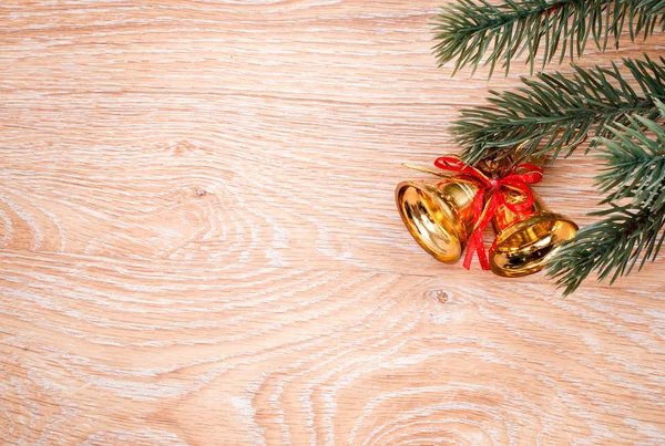 Campanas de Navidad doradas y rama de abeto sobre un fondo rústico de madera. Tarjeta de Navidad. Feliz Año Nuevo. Vista superior con espacio de copia — Foto de Stock