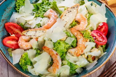 Karides salatası parmesan peyniri, kruton, domates, karışık yeşillik, marul ve ahşap arka plan üzerinde şarap ile. Maddeler tablosundaki